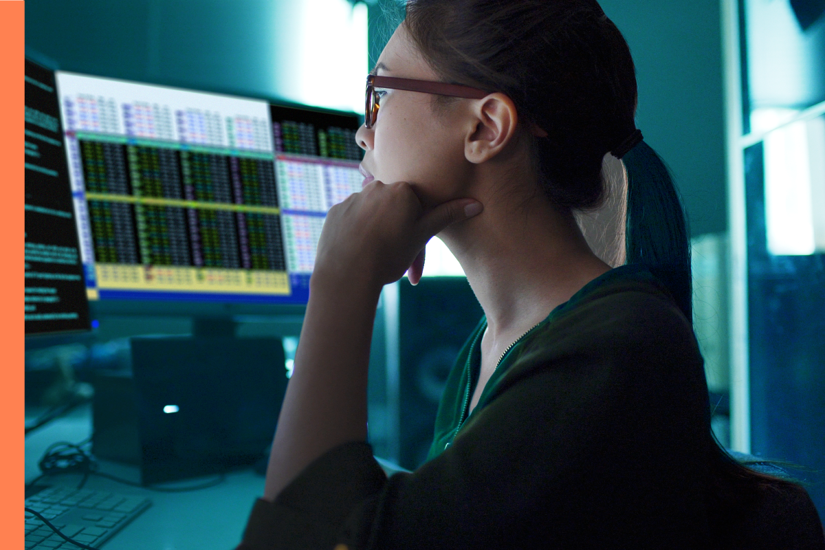 Woman with glasses sitting at a workstation with three computer screens