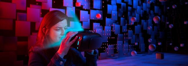 Woman looking into a VR headset against a futuristic backdrop of squares and floating circles.