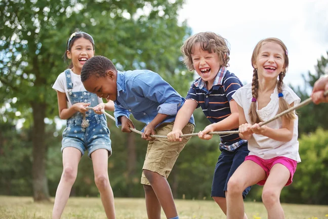 Diverse group of school-aged children pulling ropes