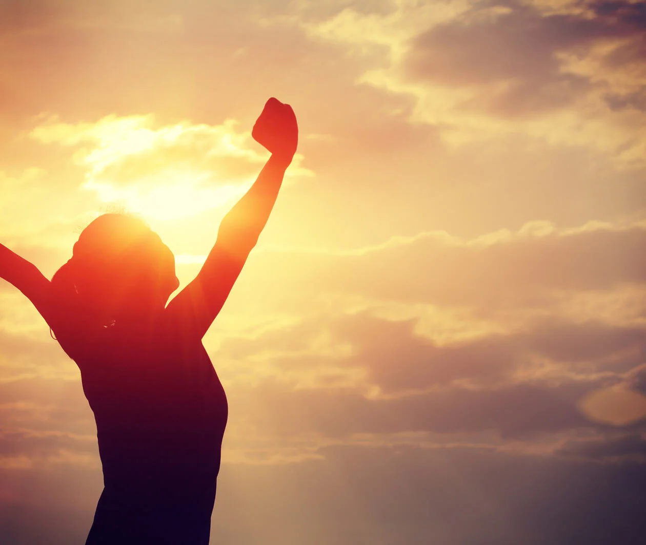 A woman raising her arms in front of a sunrise