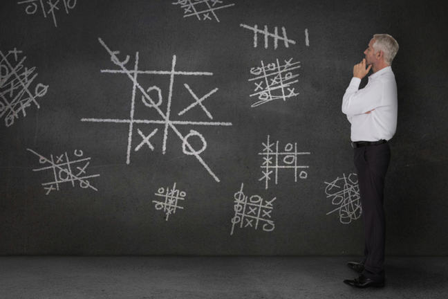 Man looking at tic tac toe games chalked on a blackboard