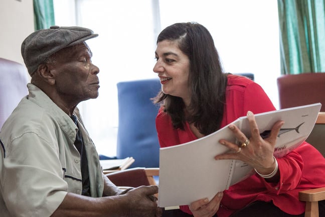 Photograph of two people talking with each other in a care home, whilst one of them holds a bound booklet