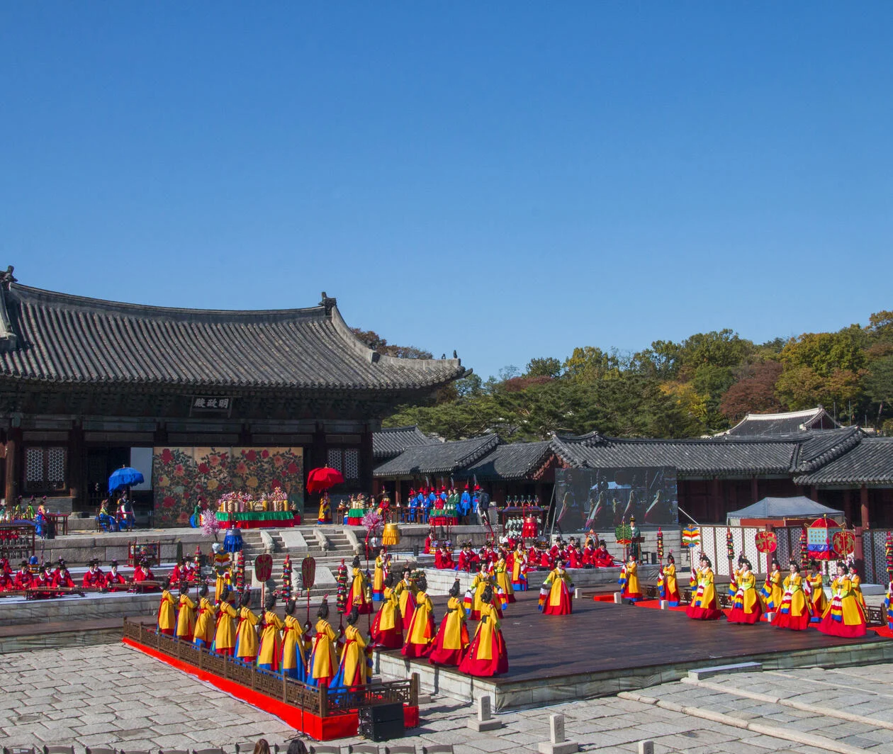 Korean royal court music: male and female performers in traditional dress stand in front of a pagoda and play music on traditional Korean instruments.