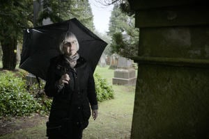 Genealogy: a lady looks at a tombstone in a graveyard while researching her family tree