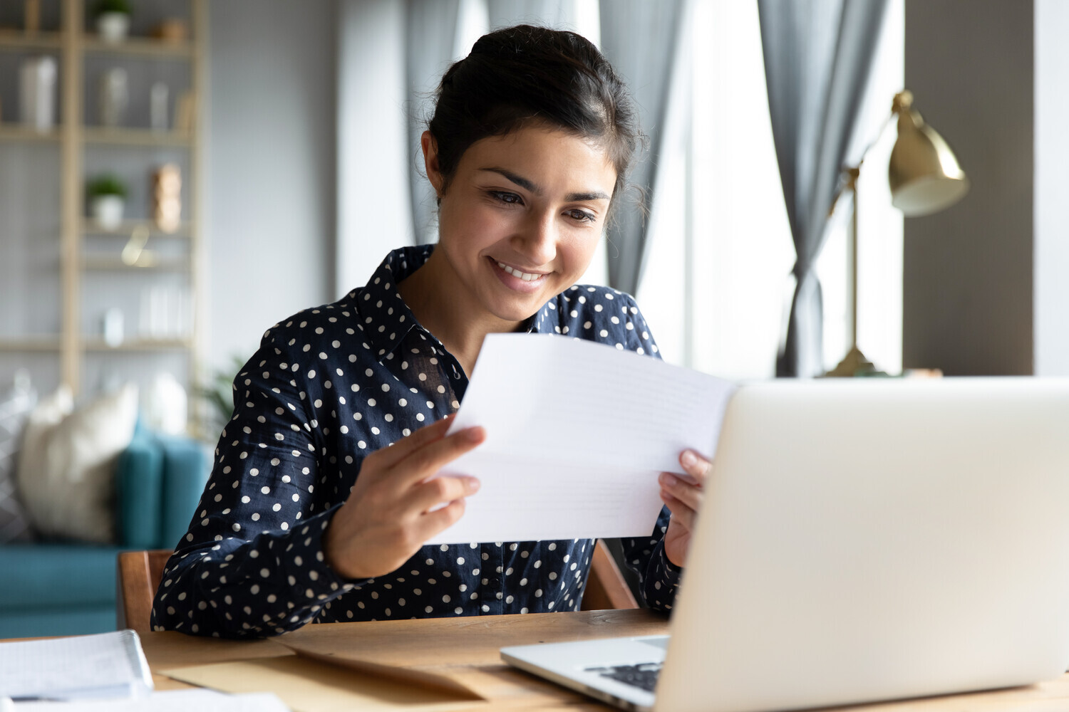 Student sat at a laptop looking at a paper document in their hands