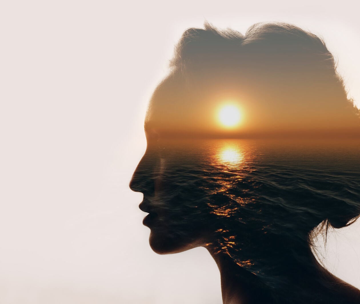 Abstract image of a sun setting over the sea within the silhouette of a woman's head