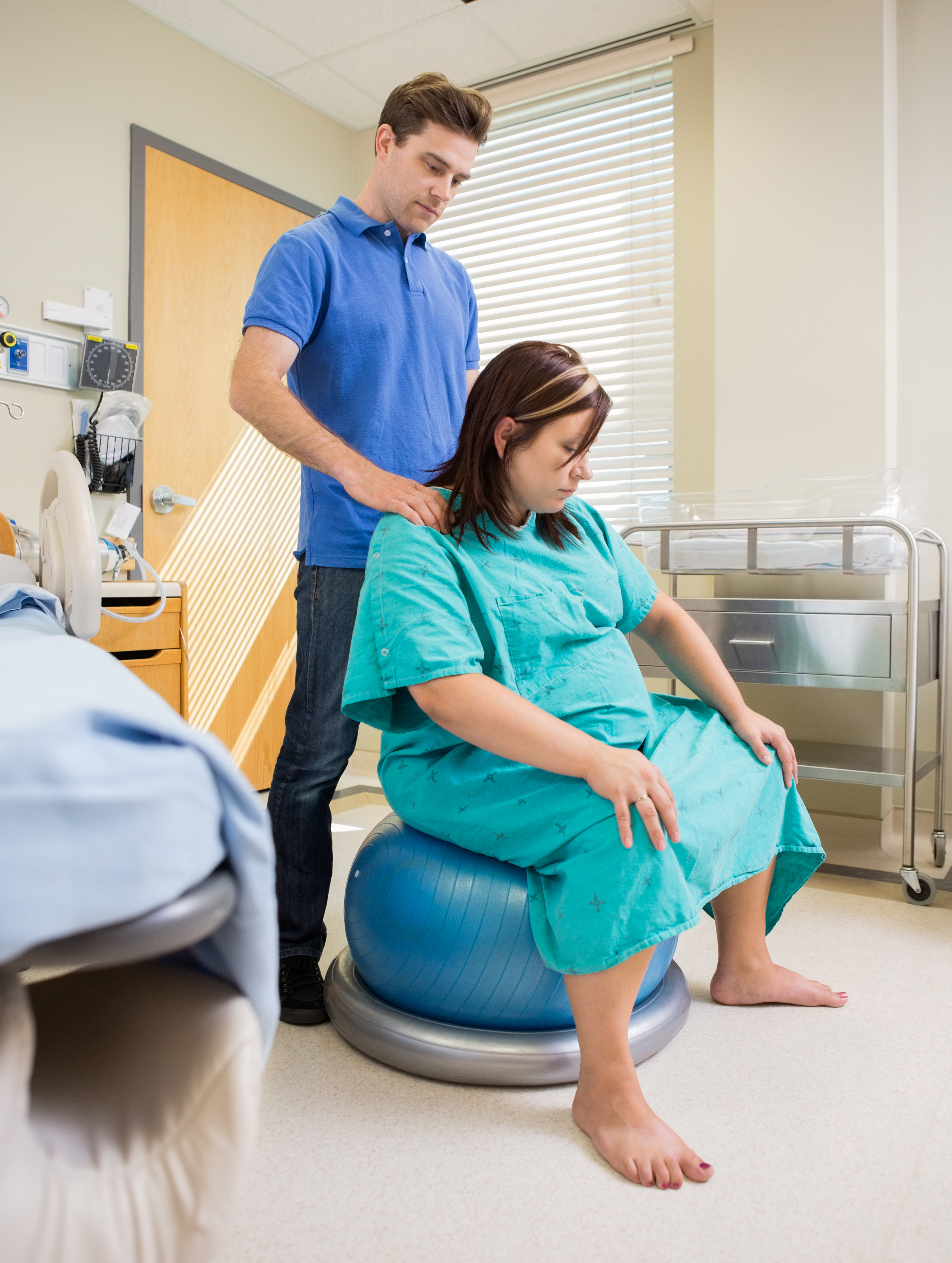 Pregnant woman in hospital sitting on exercise ball and having shoulders massaged by man