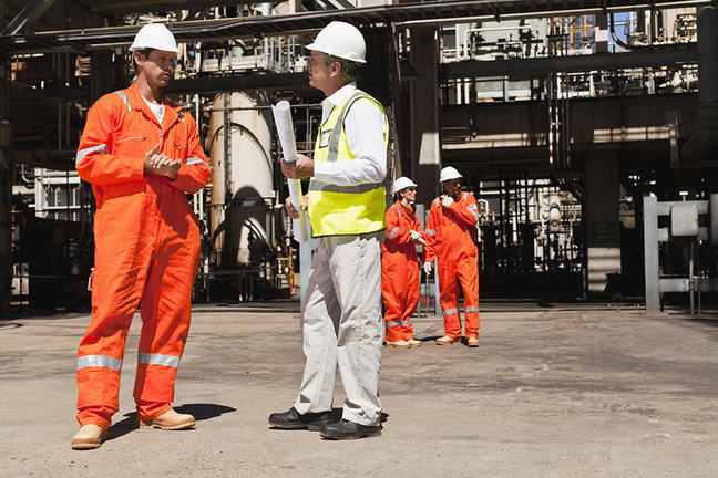 Two men in high-vis protective clothing standing near a building site.