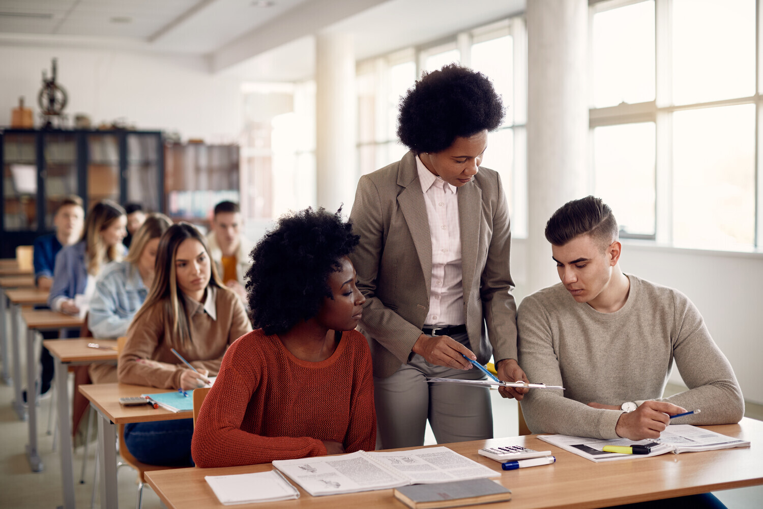 Image of two students in a class speaking to a lecturer