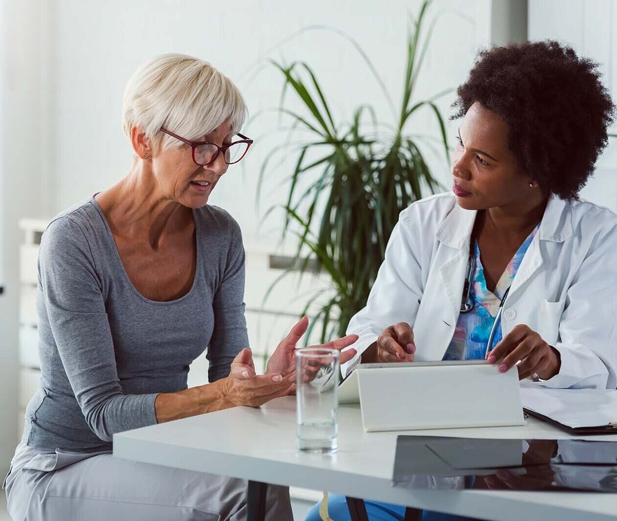 A doctor consultant her patient as they sit together talking at a desk. 