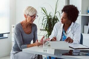 A doctor consultant her patient as they sit together talking at a desk. 