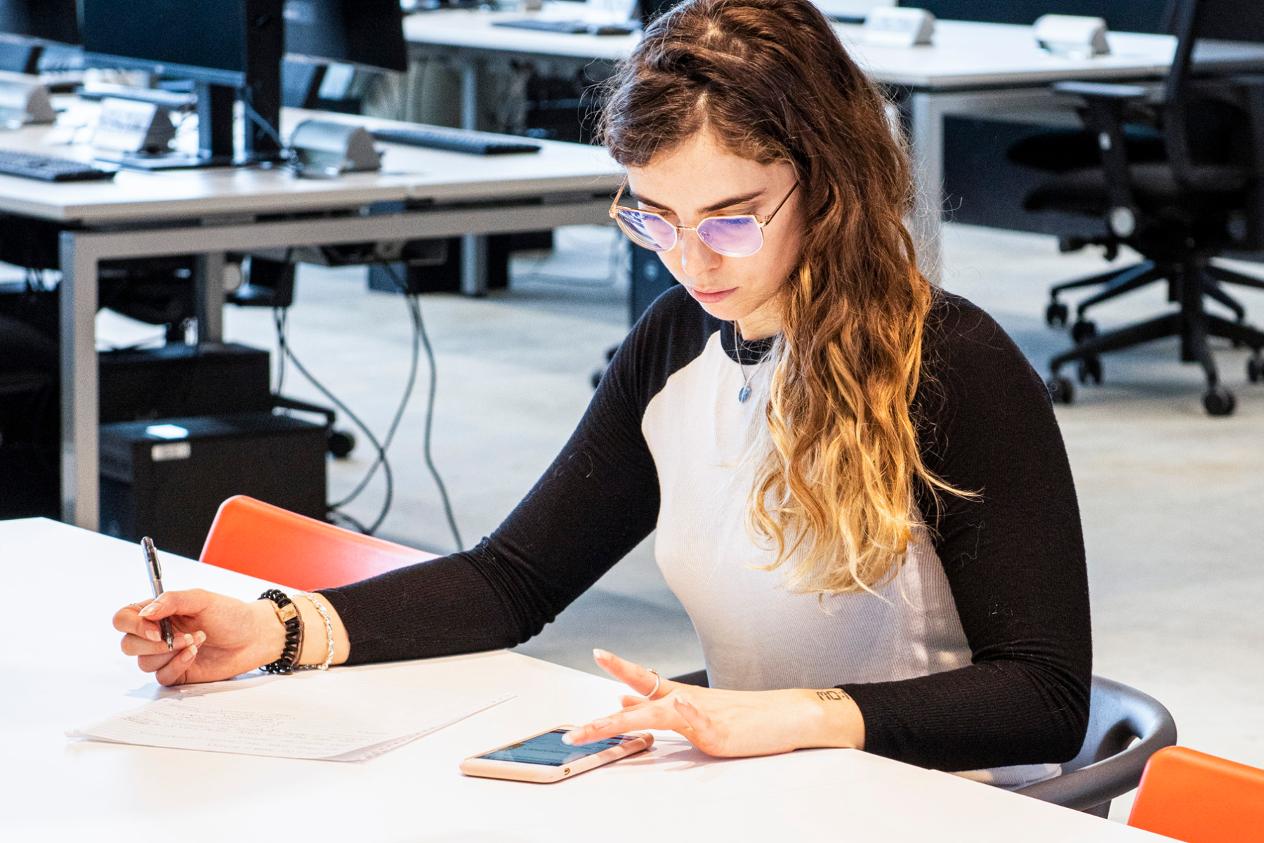 an image of someone sitting at a table reading something from their phone while taking notes.