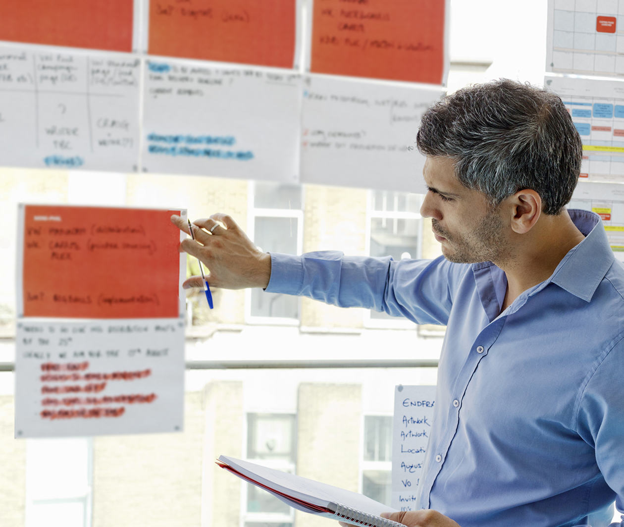 Man looking at project documentation pinned to a window, while holding a notebook.