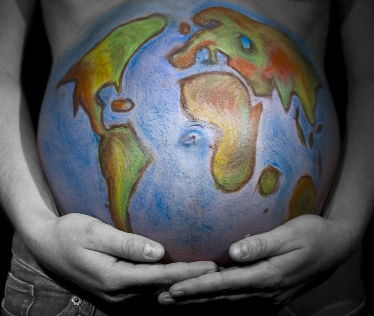 A heavily pregnant woman holds her stomach, which is painted with a map of the world