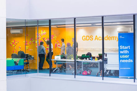 image of classroom with learners standing and looking at post its. On the wall it says GDS Academy and a sign says Start with user needs.