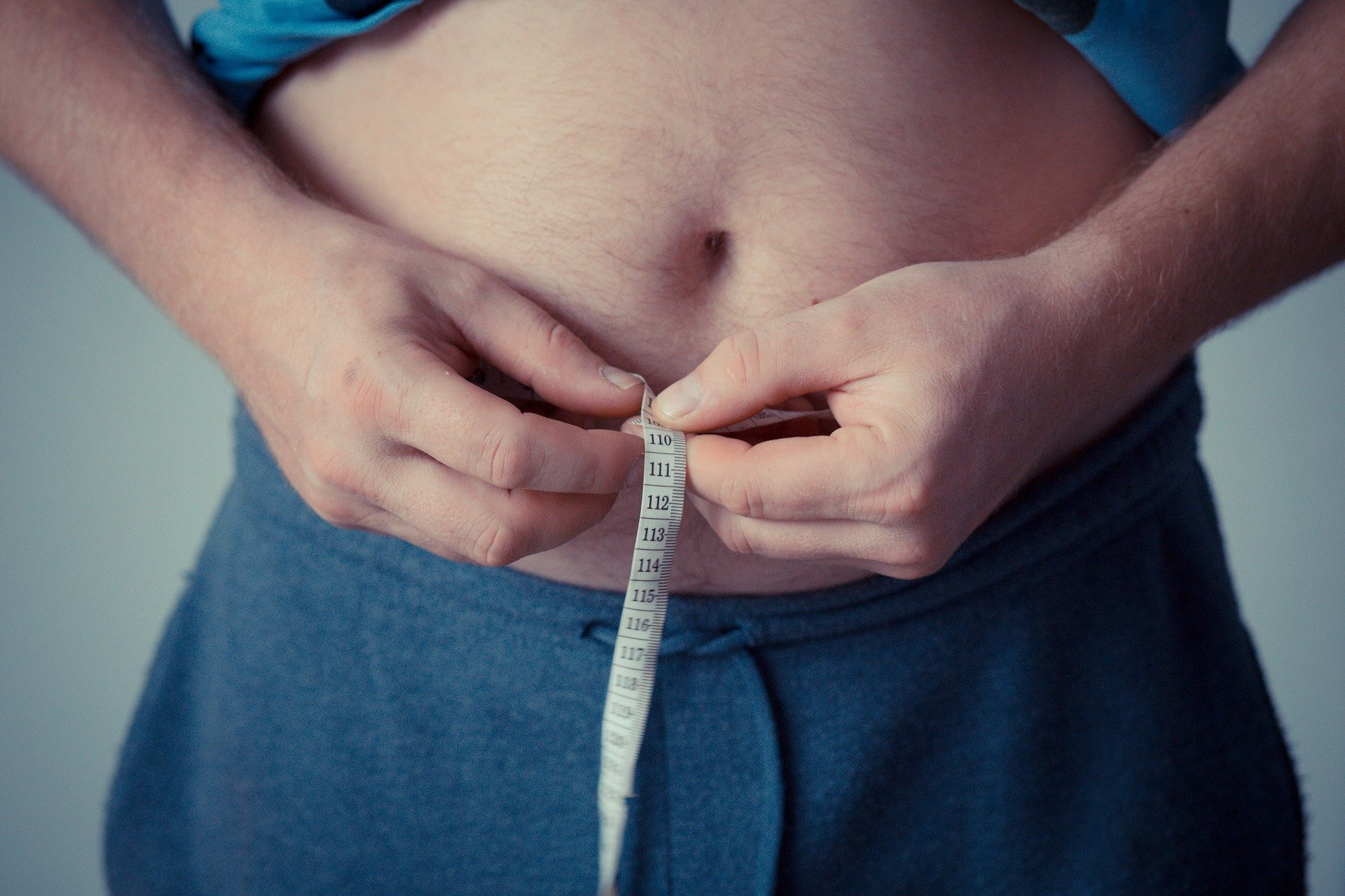 Overweight man holding measuring tape around belly