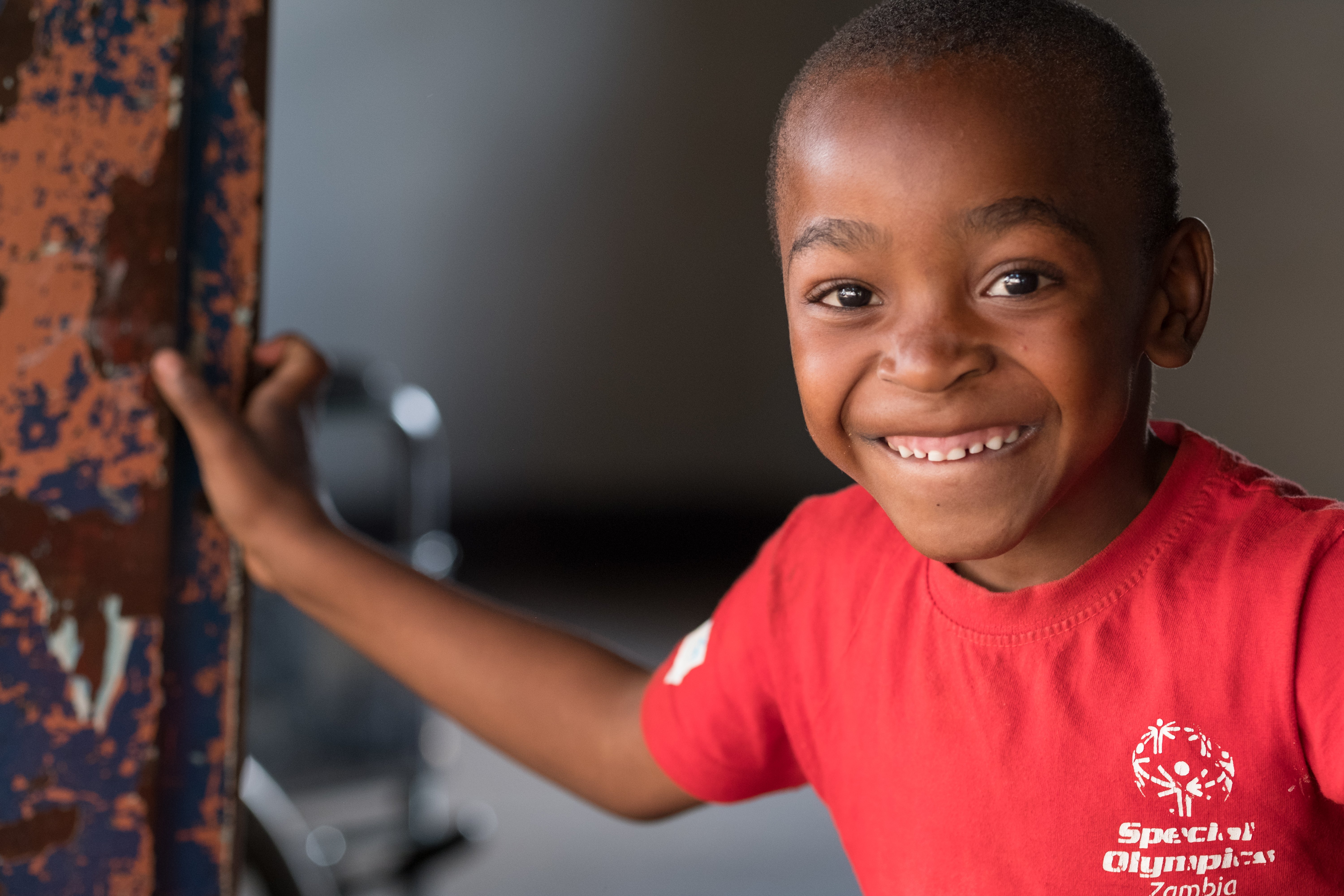 A boy is leaning against a metal pole as he smiles at the camera.