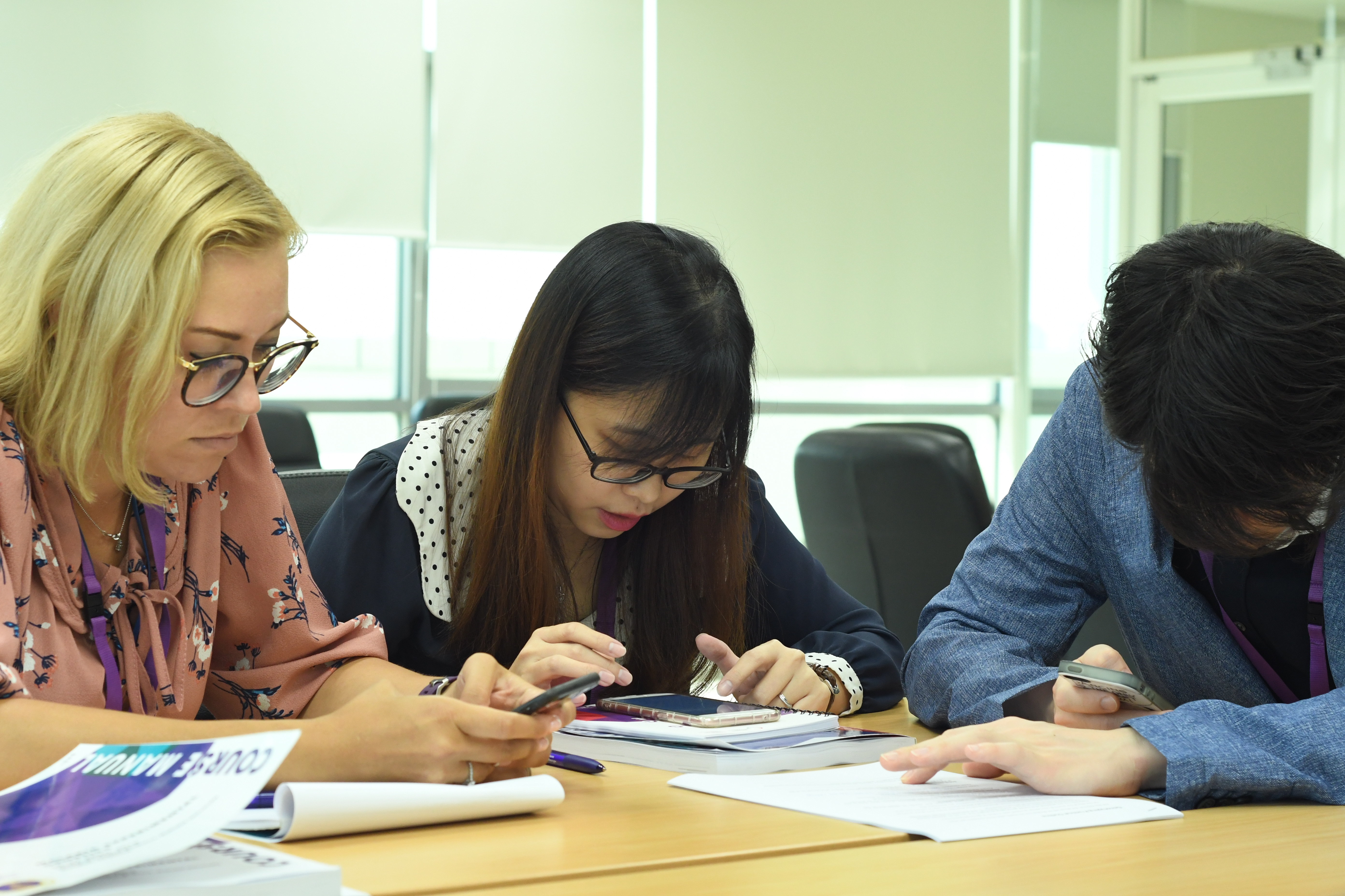 Three learners sitting at a desk and concentrating on some work involving use of phones