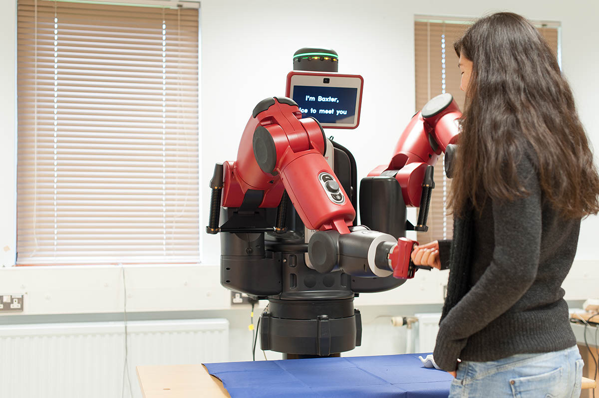 A University of Reading student meeting a Baxter robot. She 'shakes' the robot's 'hand' and on the screen it says, 'I'm Baxter, nice to meet you'.