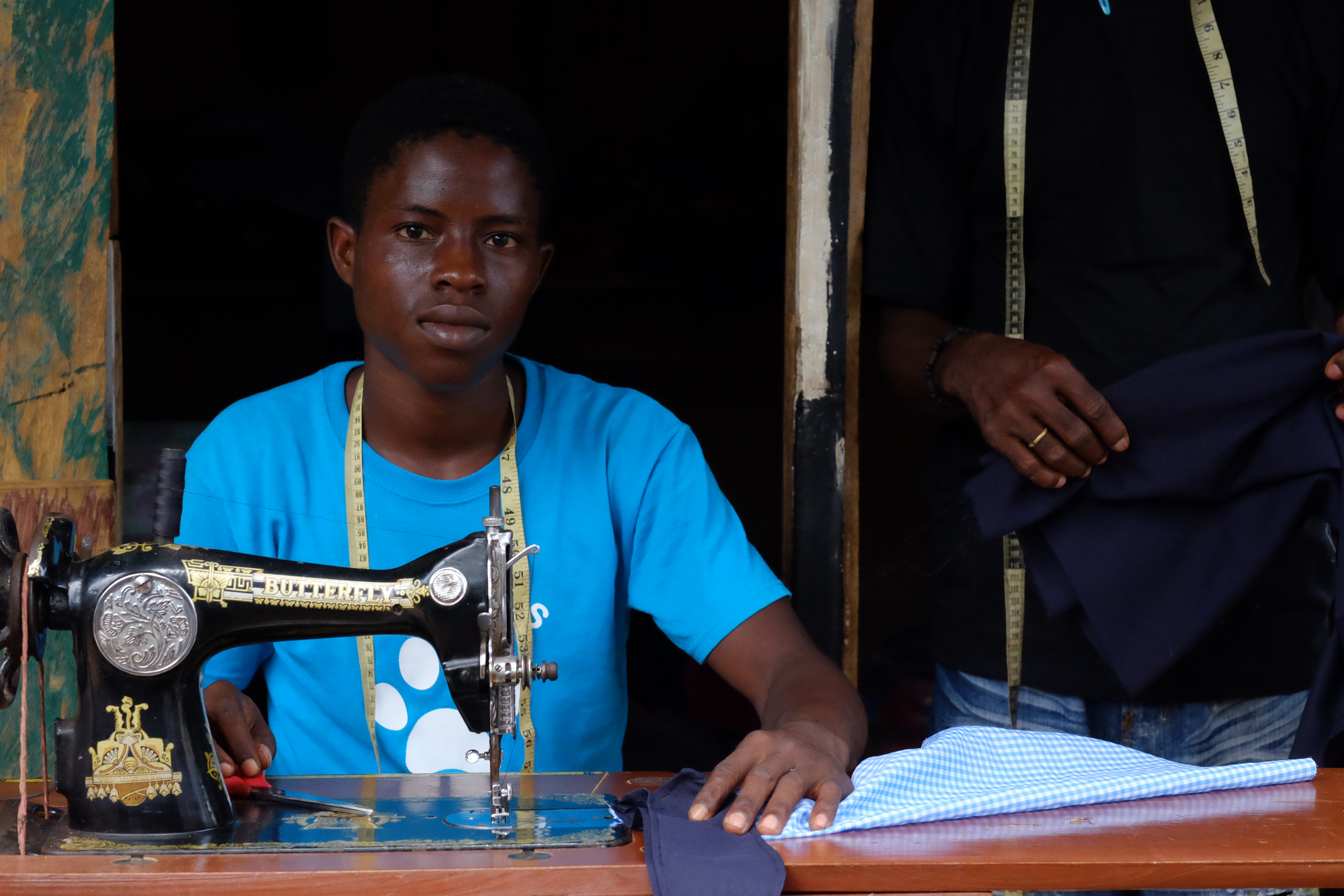 a young tailor looking straight at the camera sitting behind his sewing machine