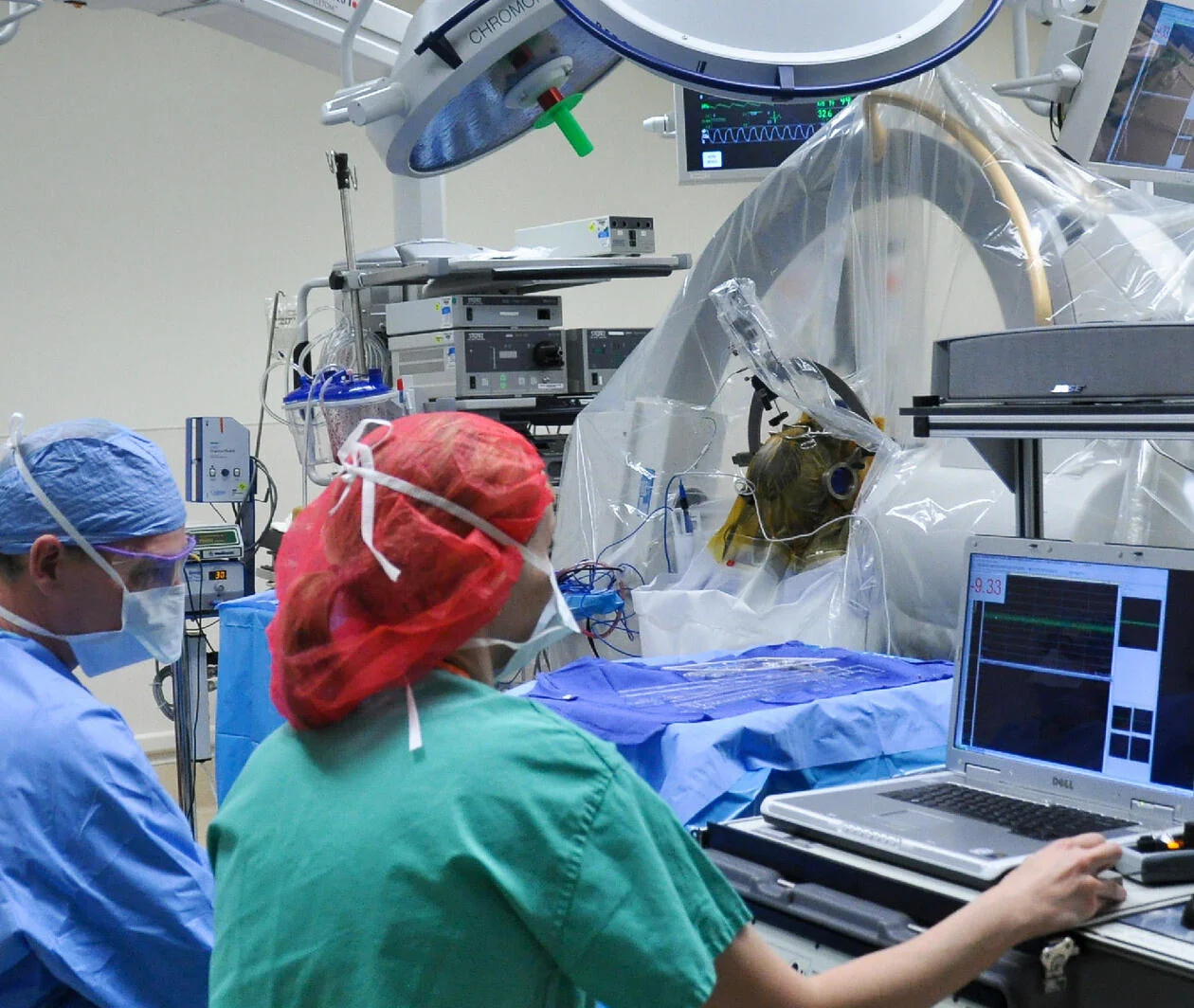 Scene from a surgical procedure with three medical professionals in full surgical garb and a patient undergoing a scan.