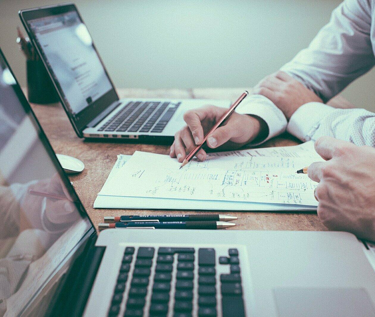 Photo of an office desk with two colleagues planning using laptops and paper.