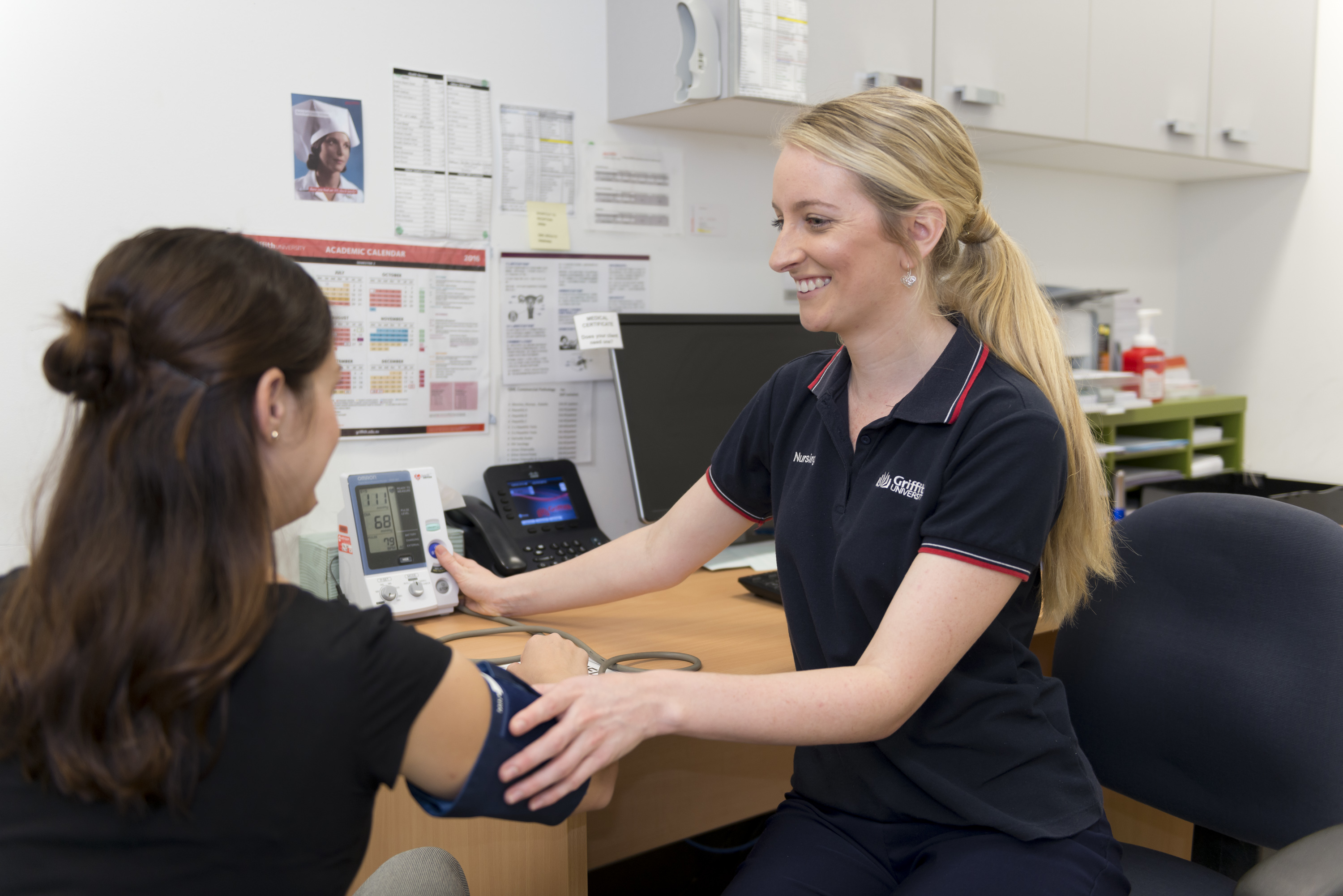 A smiling health care practitioner sits to take the blood pressure of her client.