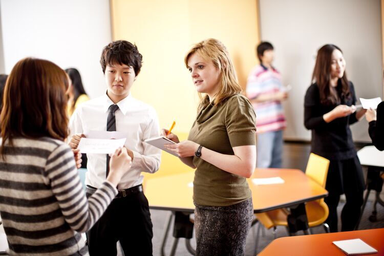 Teacher assessing students and taking notes while they present to classmates