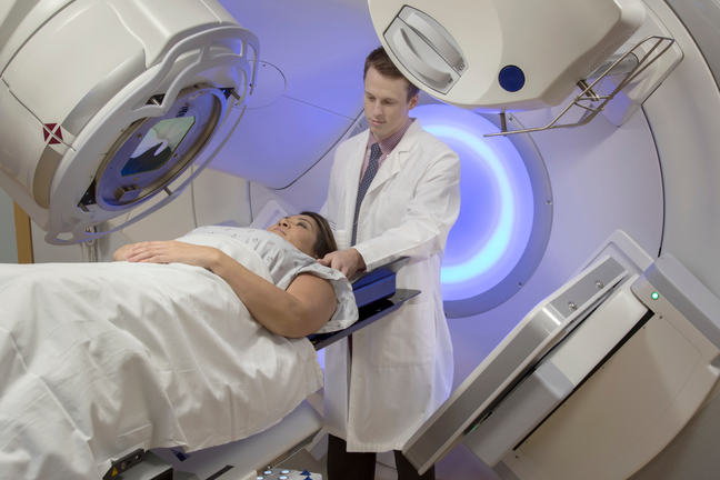 A patient undergoing radiation therapy with a radiation therapy standing beside her