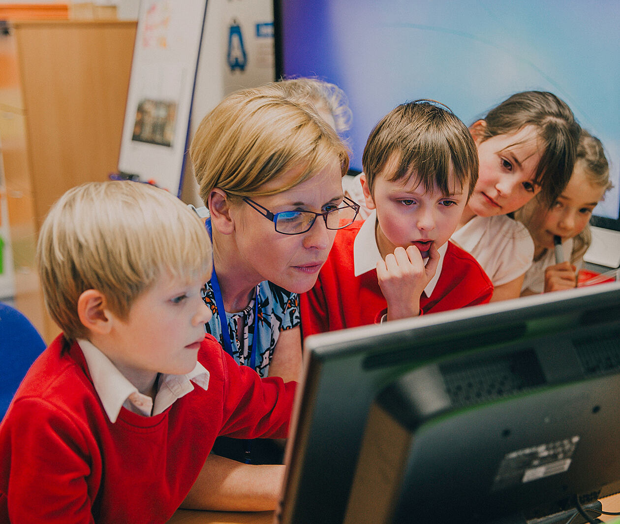 A class watch a film intently while surrounded by literacy prompts.