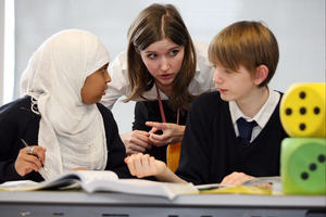 Teacher leaning in to speak to two teenaged students.