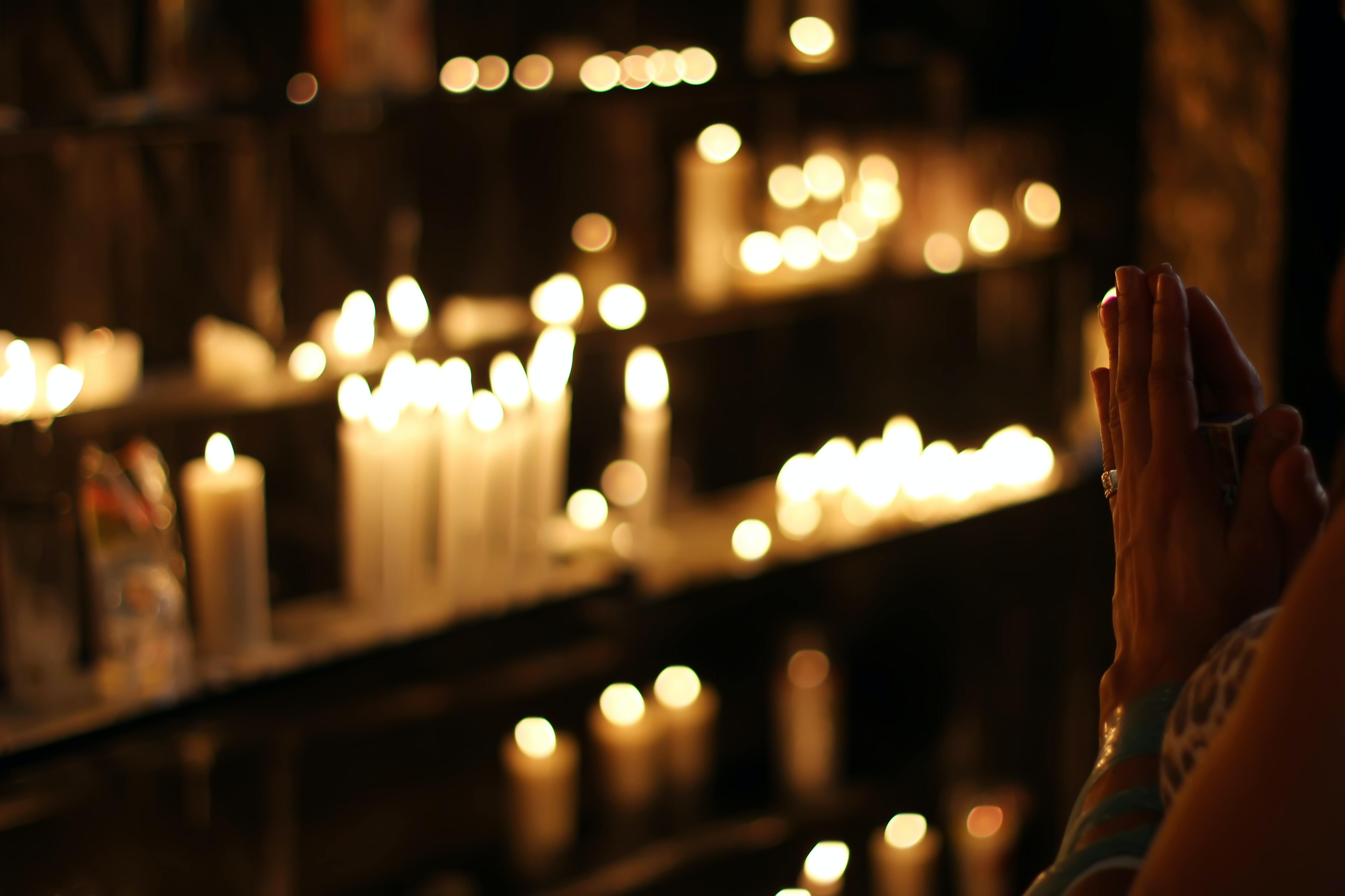 Hands joined in prayer in front of lit candles.