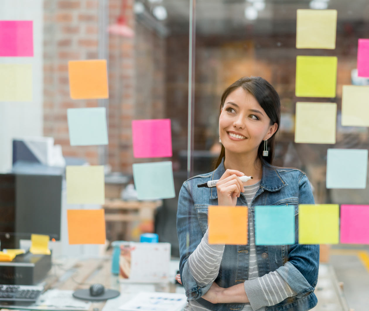 Woman uses sticky notes on a glass wall to analyse data drawn from qualitative research.