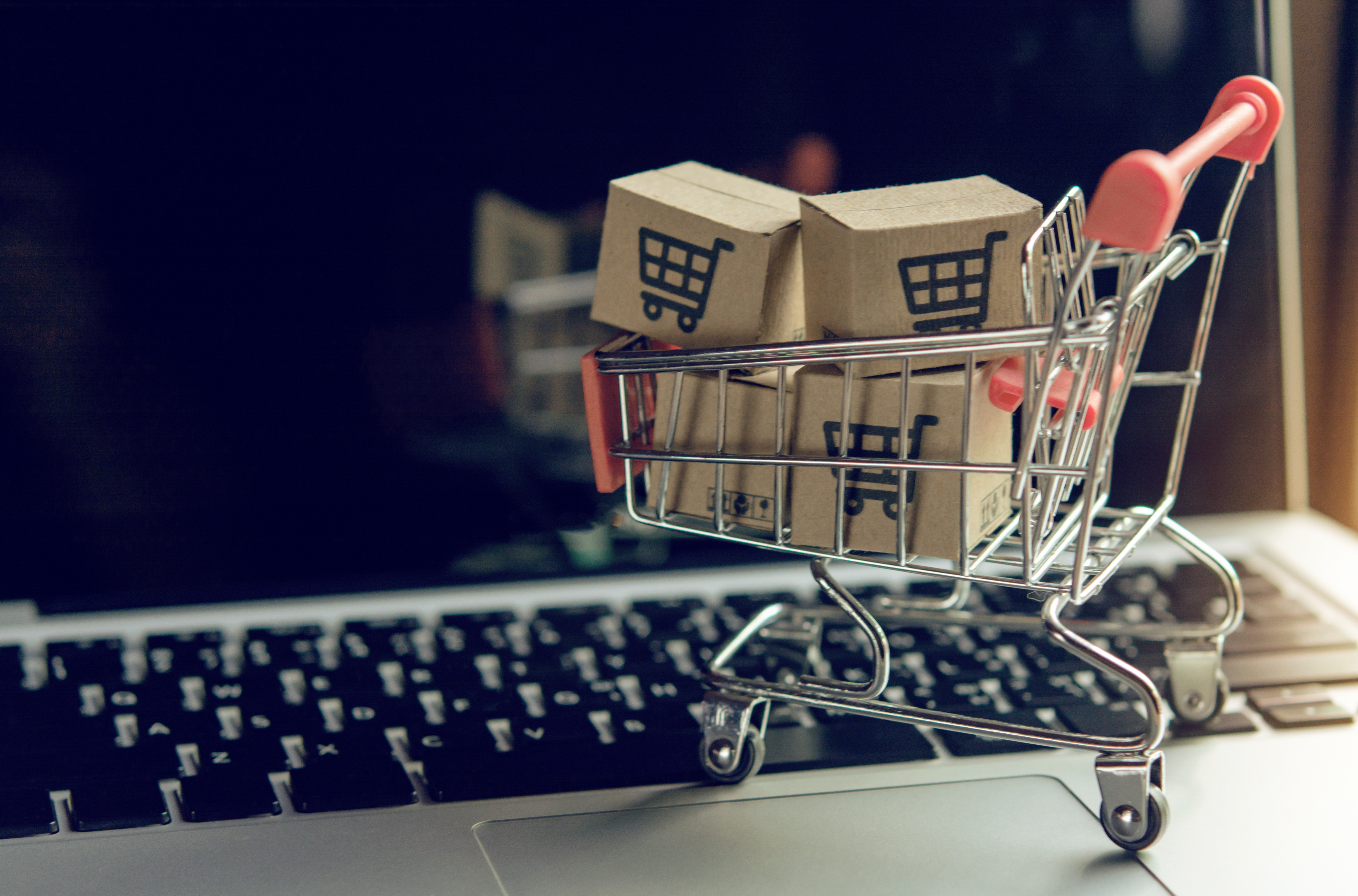 an mini shopping trolley full of mini boxes, rolling on an opened laptop