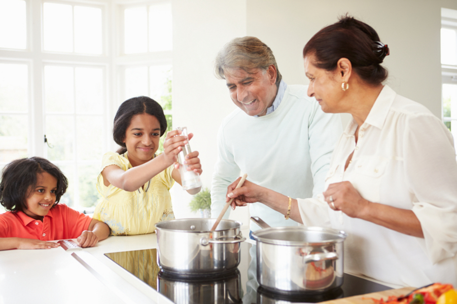 A family of two children and a man and woman cooking in a kitchen with silver pots.