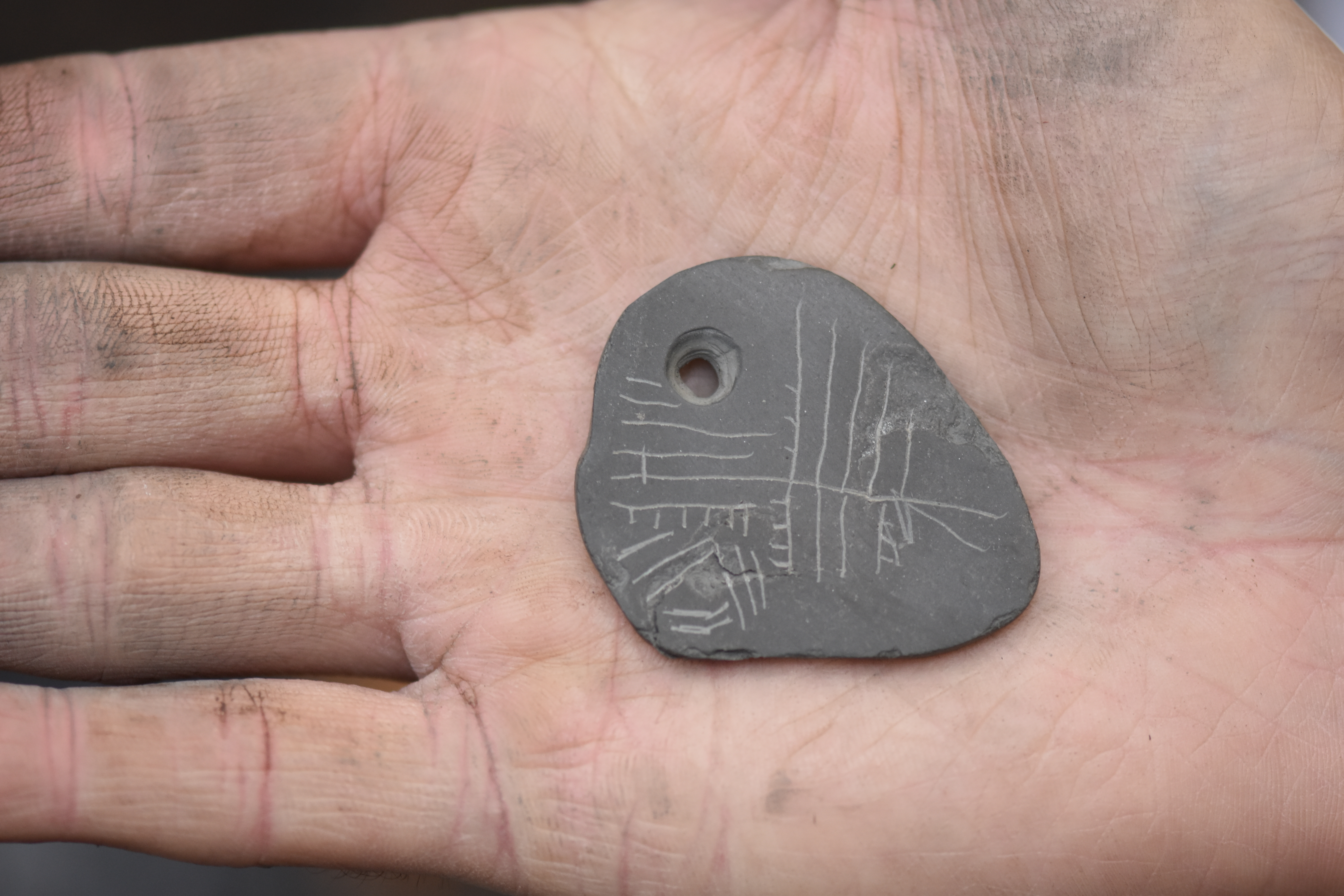 A replica shale pendant with lines scratched into the surface which show up as white