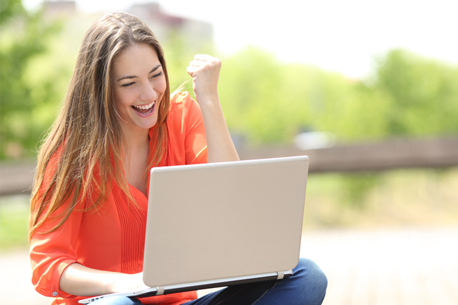 Delighted woman punching the air while working at a laptop