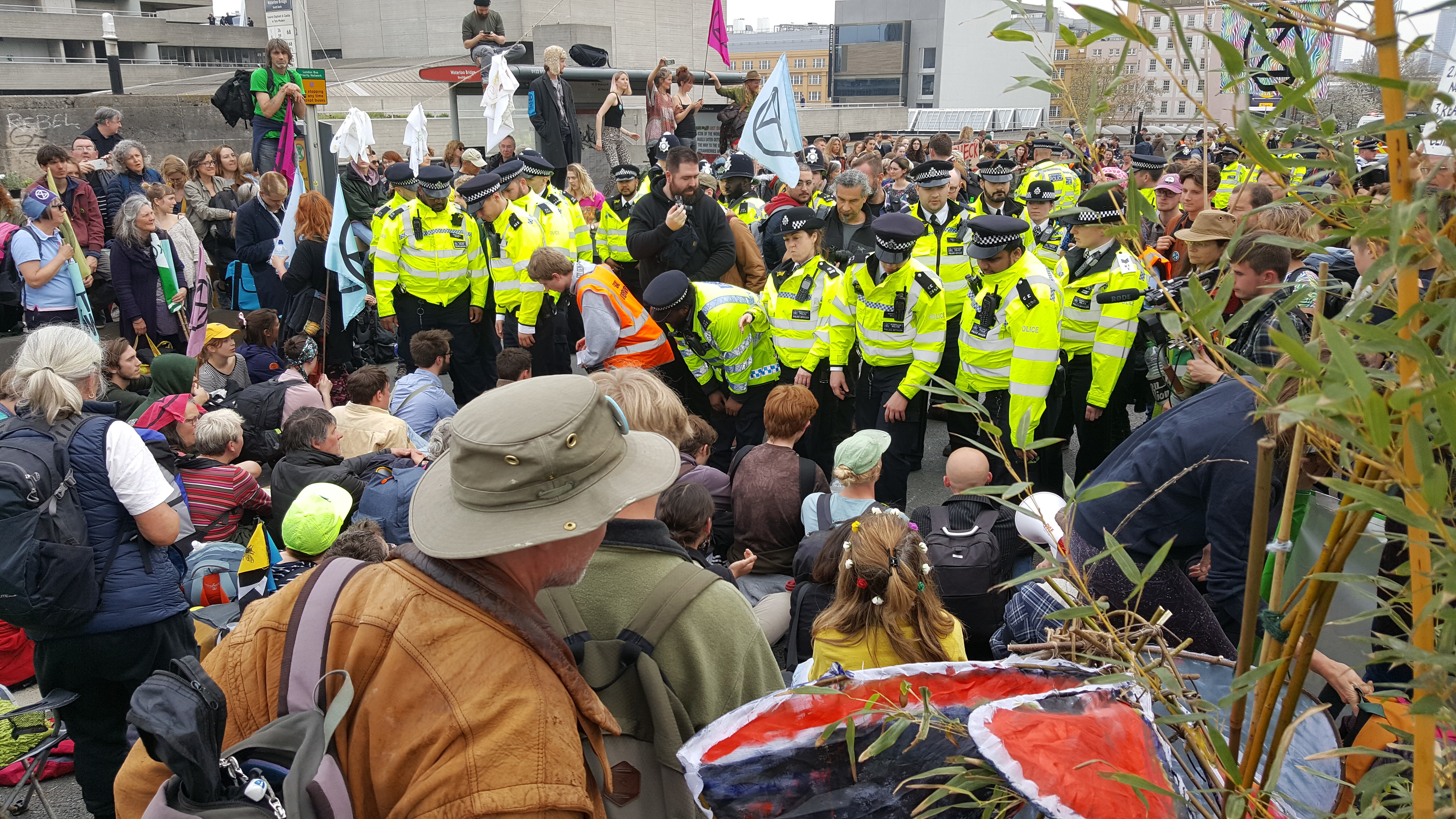 A line of police face a crowd of protestors sat on the ground.