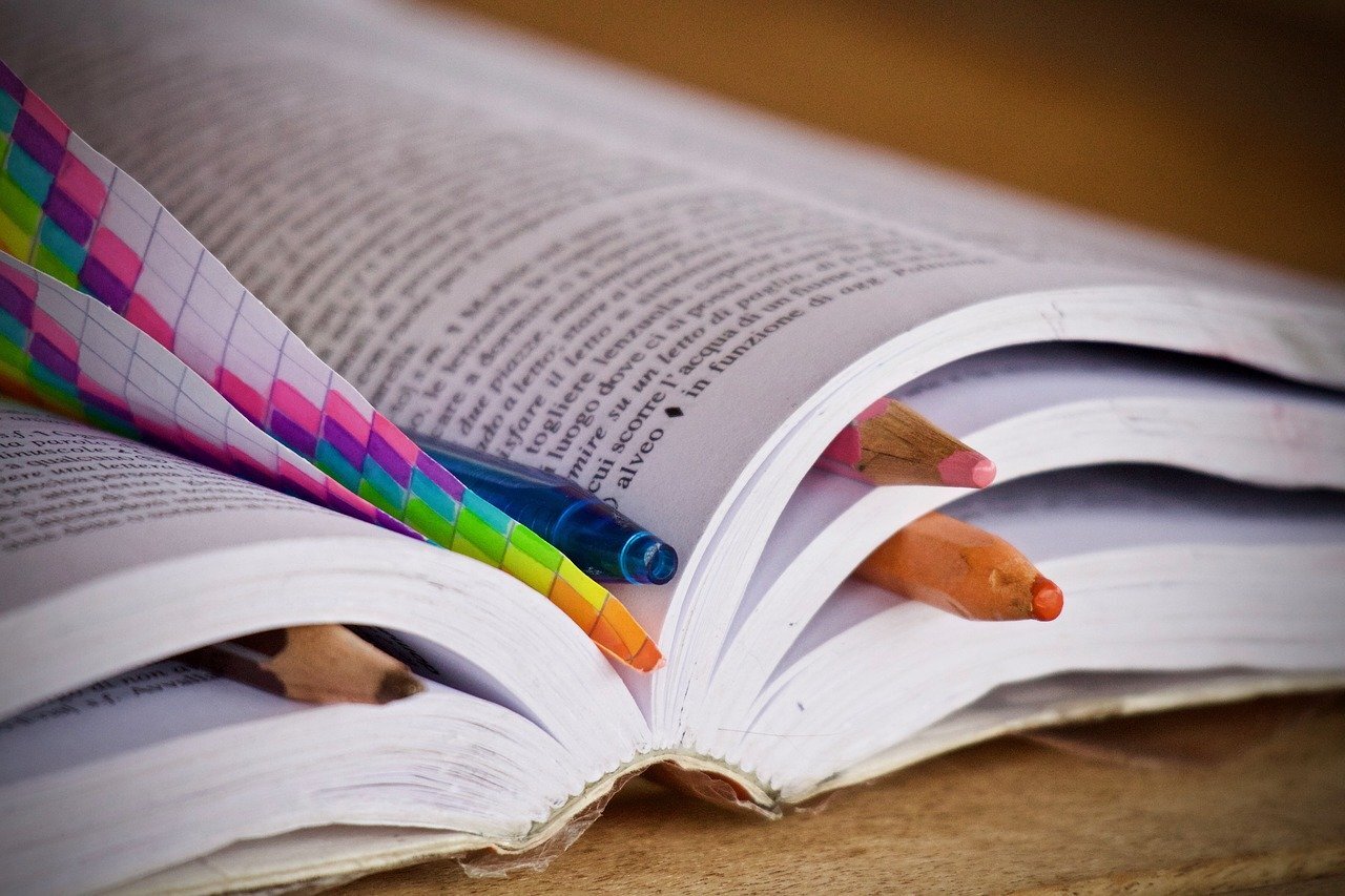 A book lying open on a desk with several places marked with pencils and pieces of paper slid between the pages