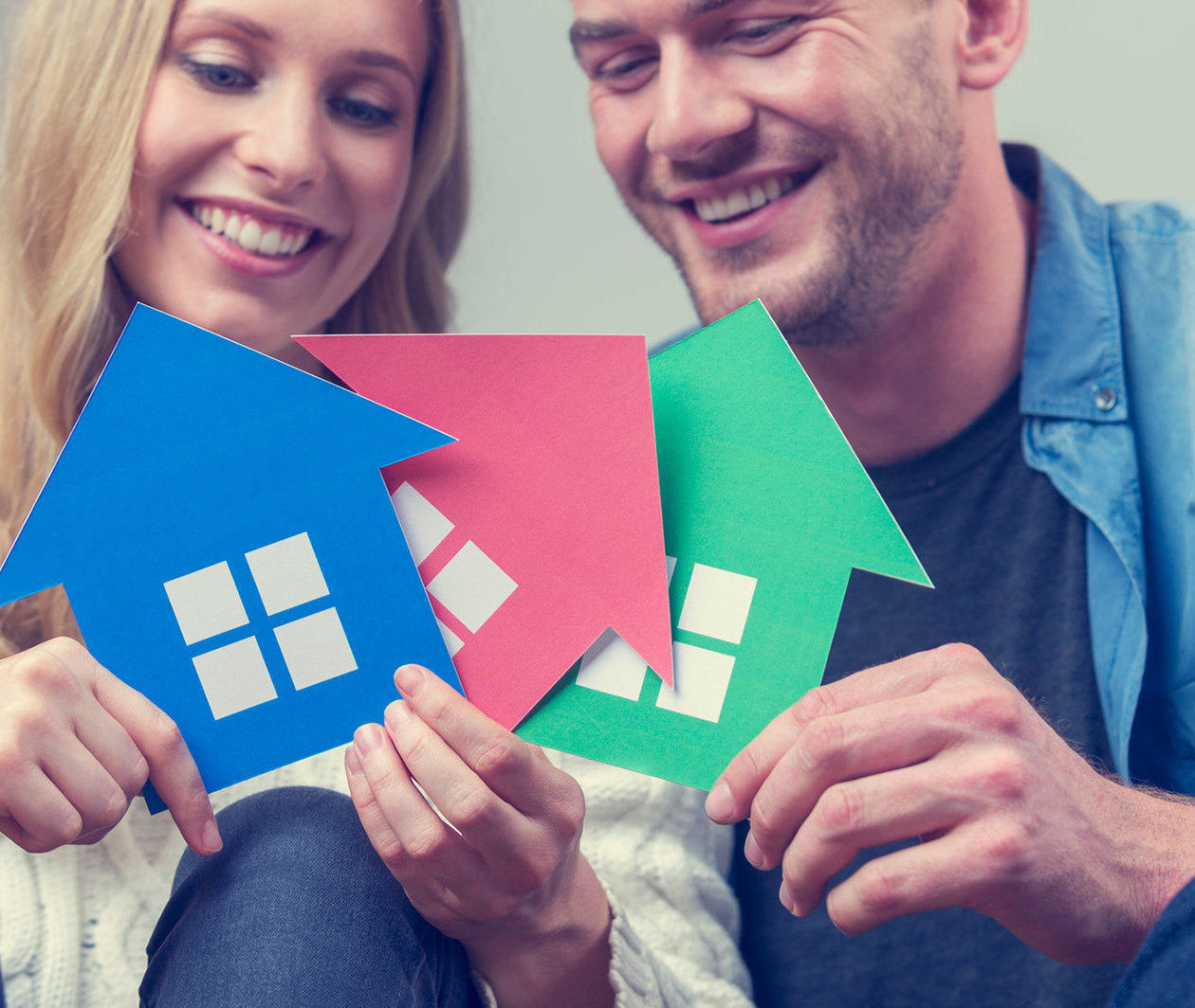 Young couple holding up cardboard houses of different colours.