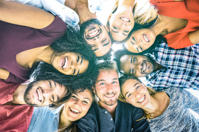 This image shows a group of young people from different cultures in a circle with their arms around each other, looking down at the camera.