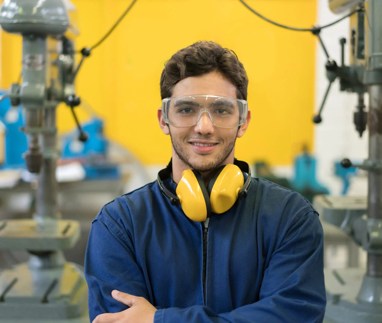 a young man working in STEM standing in a factory wearing protective glasses and yellow ear muffs