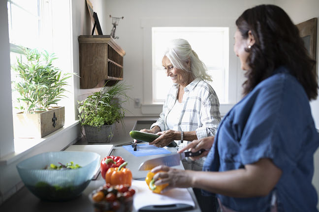 Daughter and senior mother cooking, cutting vegetables in kitchen