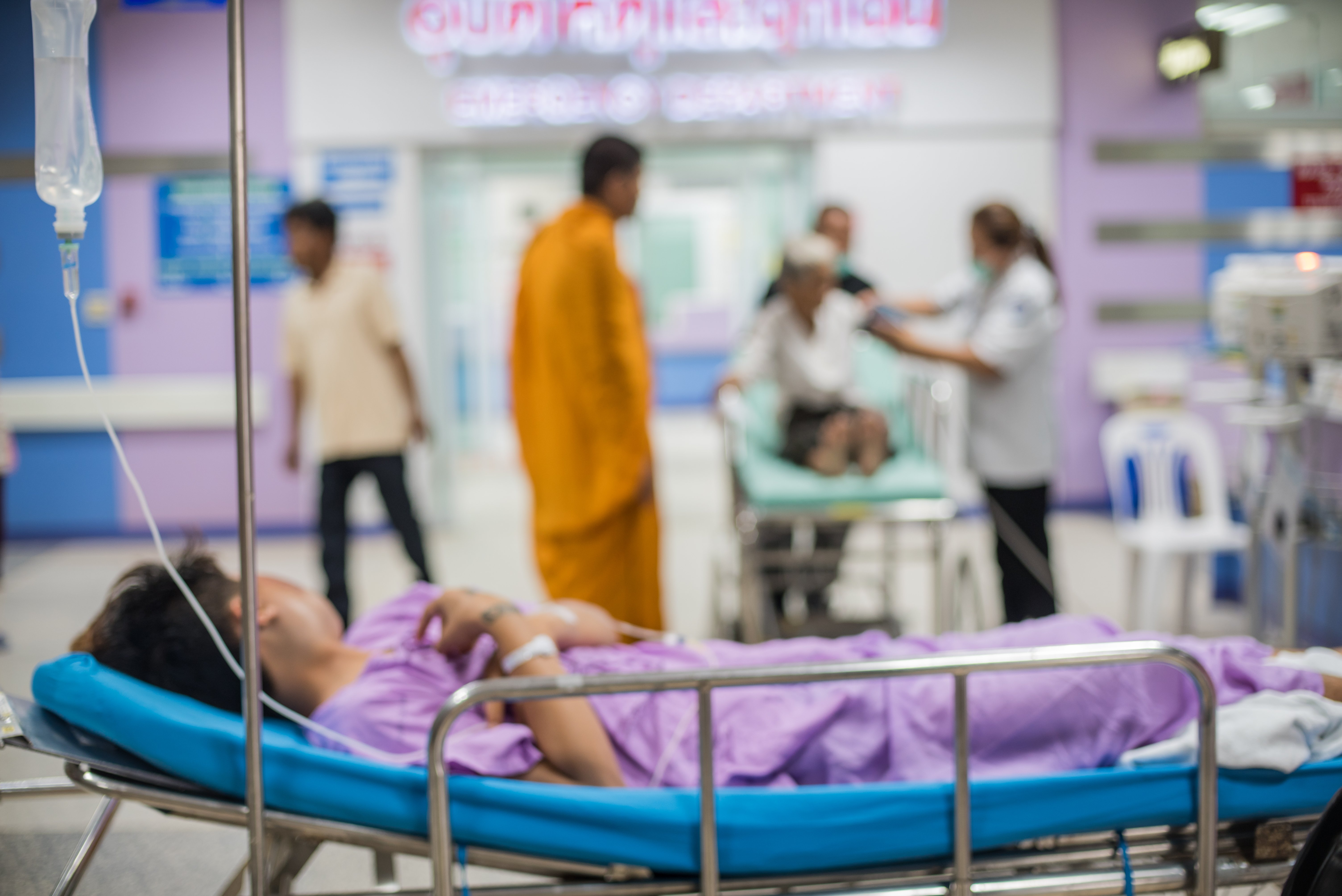 The image shows a blurred hospital background with a patient on a bed