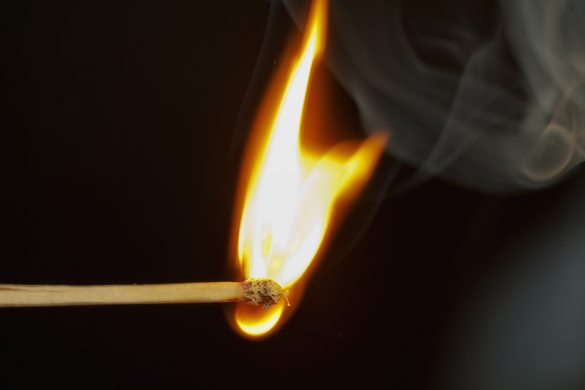 A match stick on fire, burning a yellow flame. There is smoke rising from the end of the stick too.