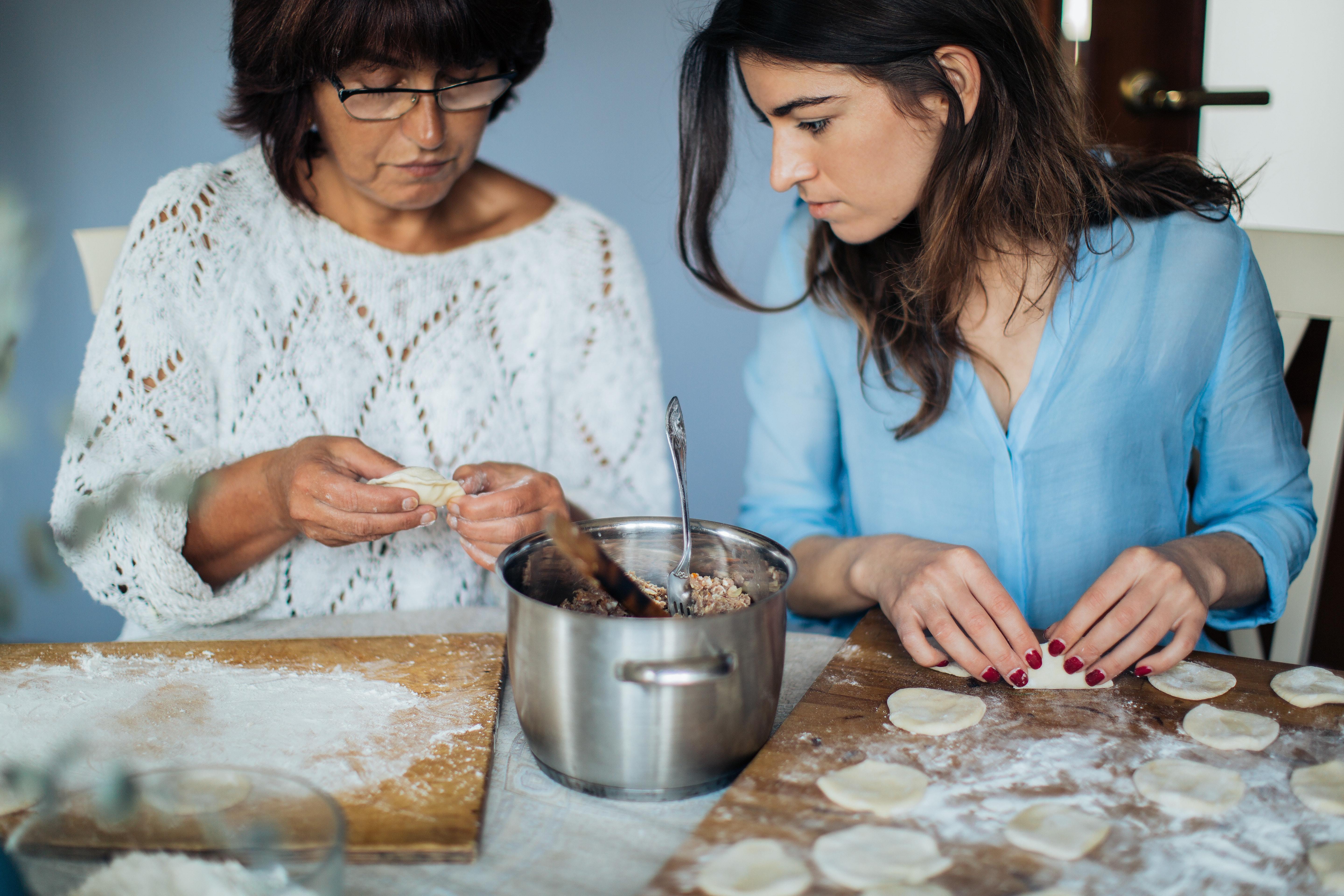 Two women making dumplings. The young person is watching what the older person does.