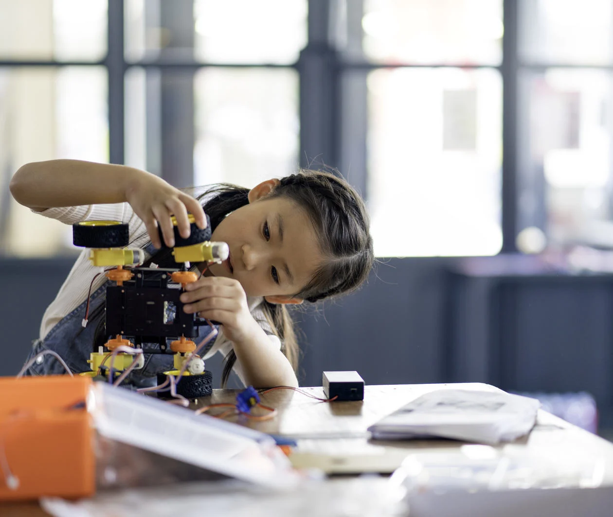 A young girl tilts her head to one side as she works on building a small robot.