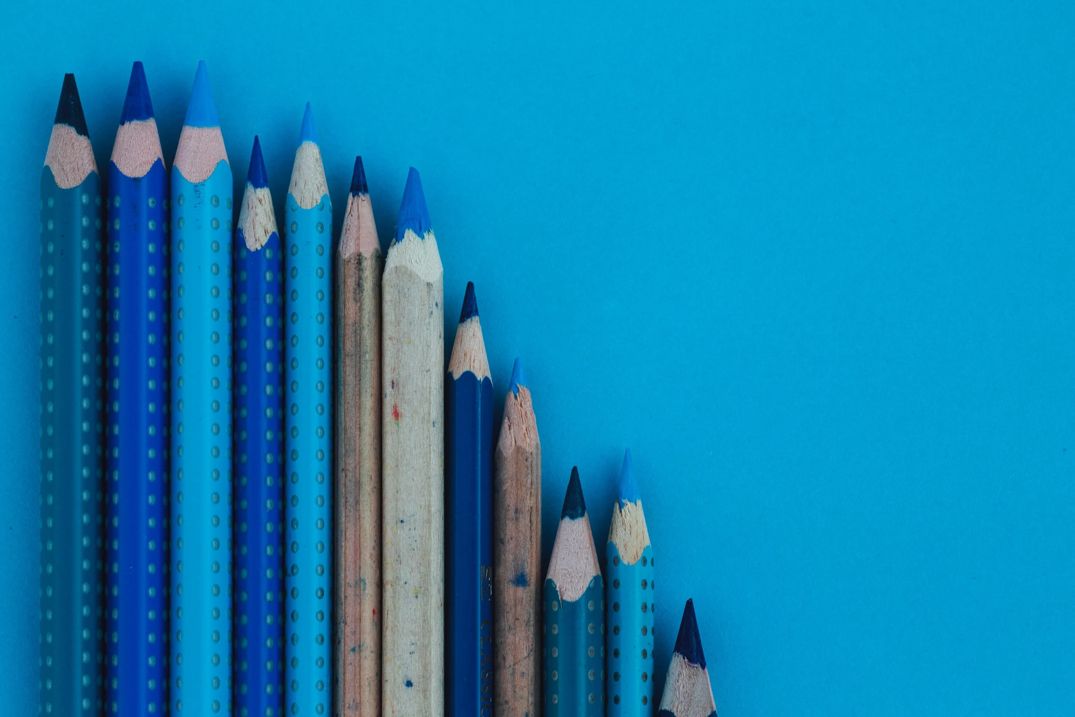 Selection of different length and different tone blue colouring pencils on a blue background