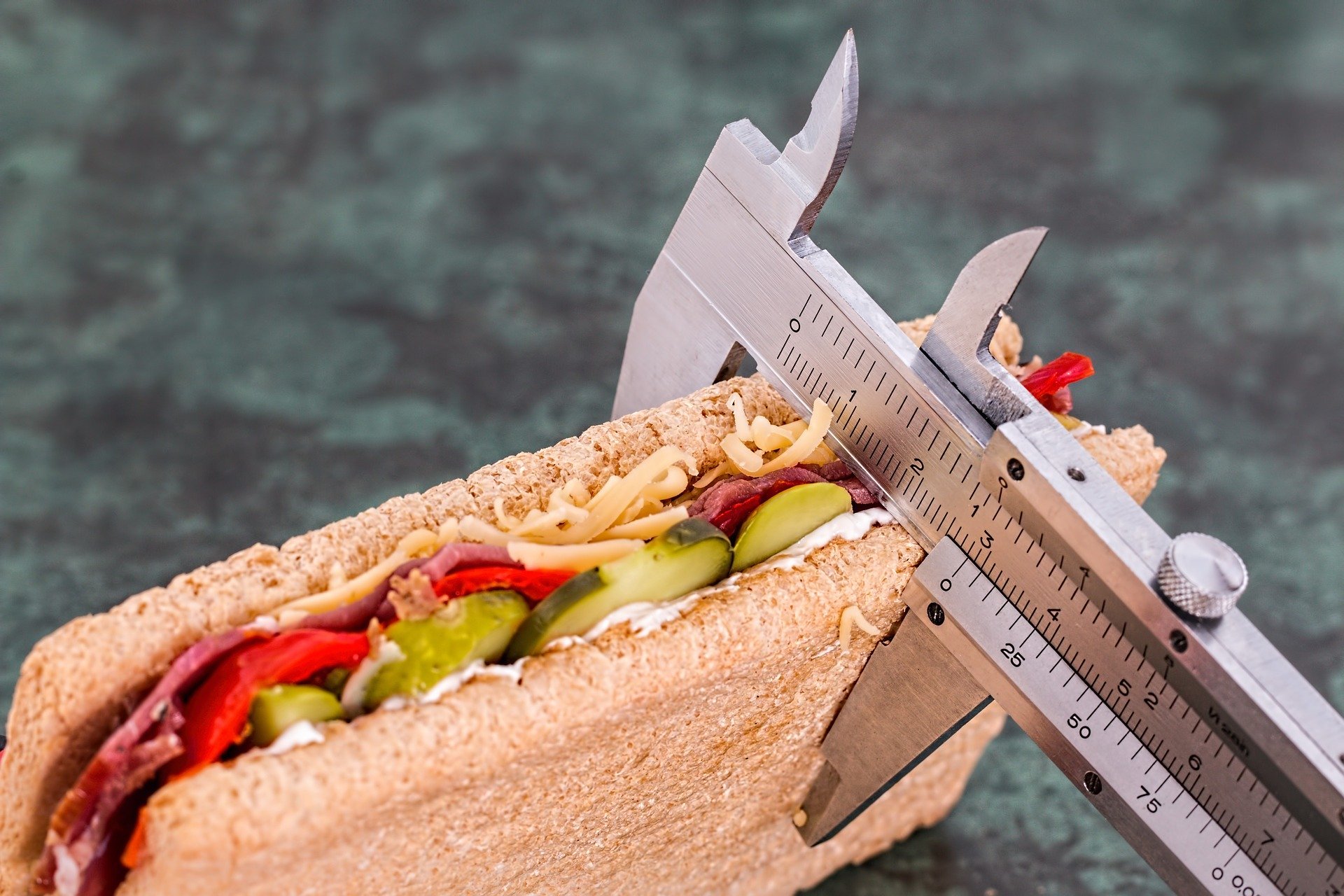 Photograph of the width of a sandwich containing cheese, tomato, ham and cucumber being measured by a caliper