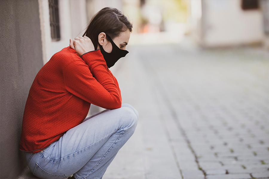 A young woman wearing a surgical mask looking sad